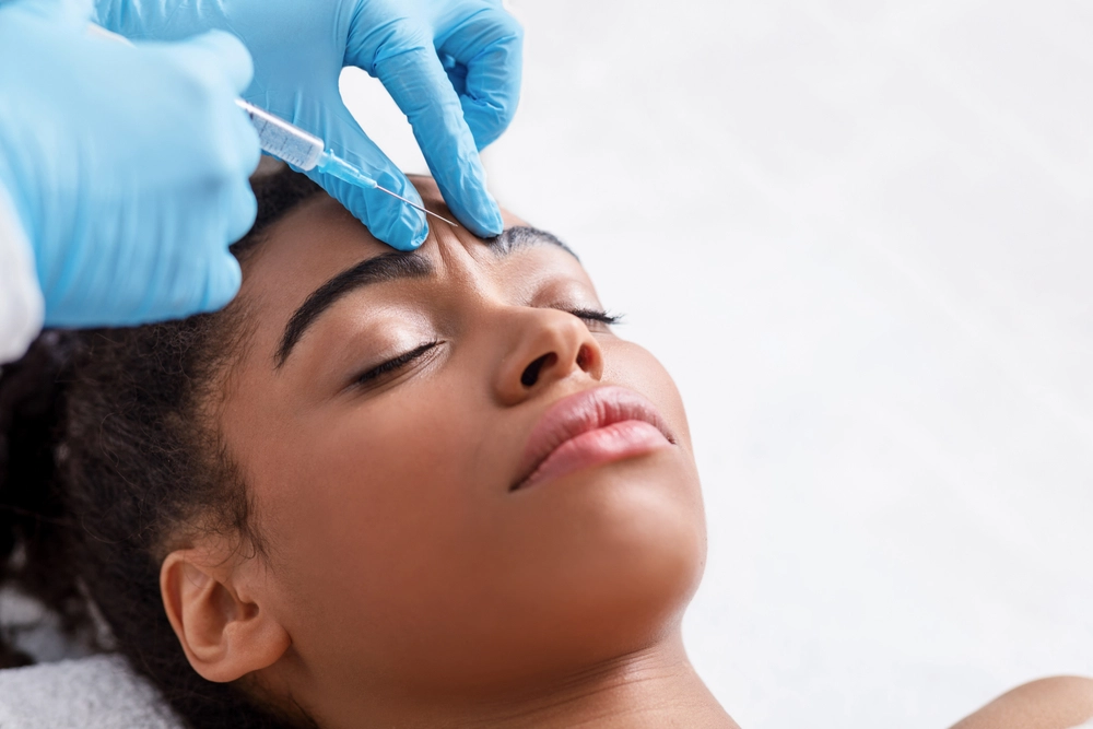 Plastic surgery. Young african woman receiving botox injection in interbrow zone at beauty clinic, closeup, copy space